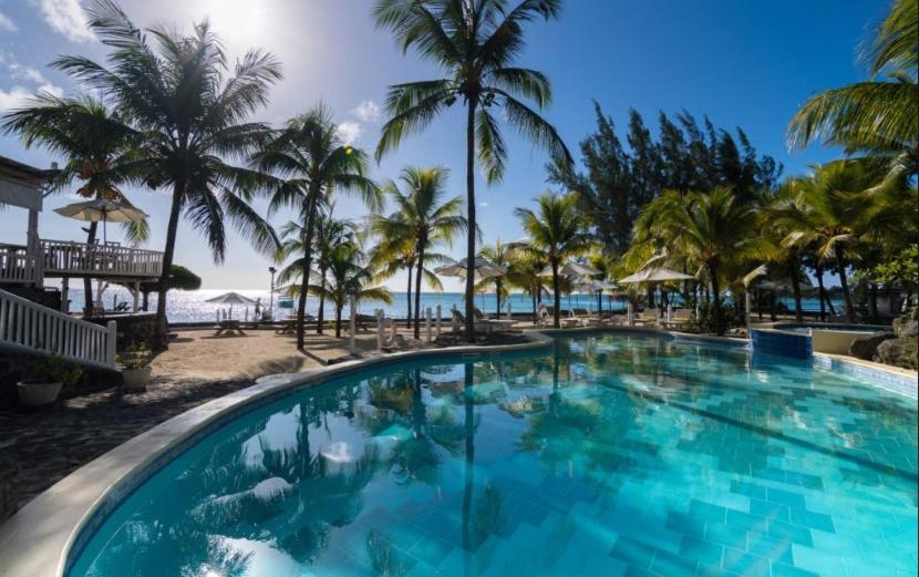 a swimming pool at a resort with palm trees and the ocean at Hibiscus Boutique Hotel in Pereybere