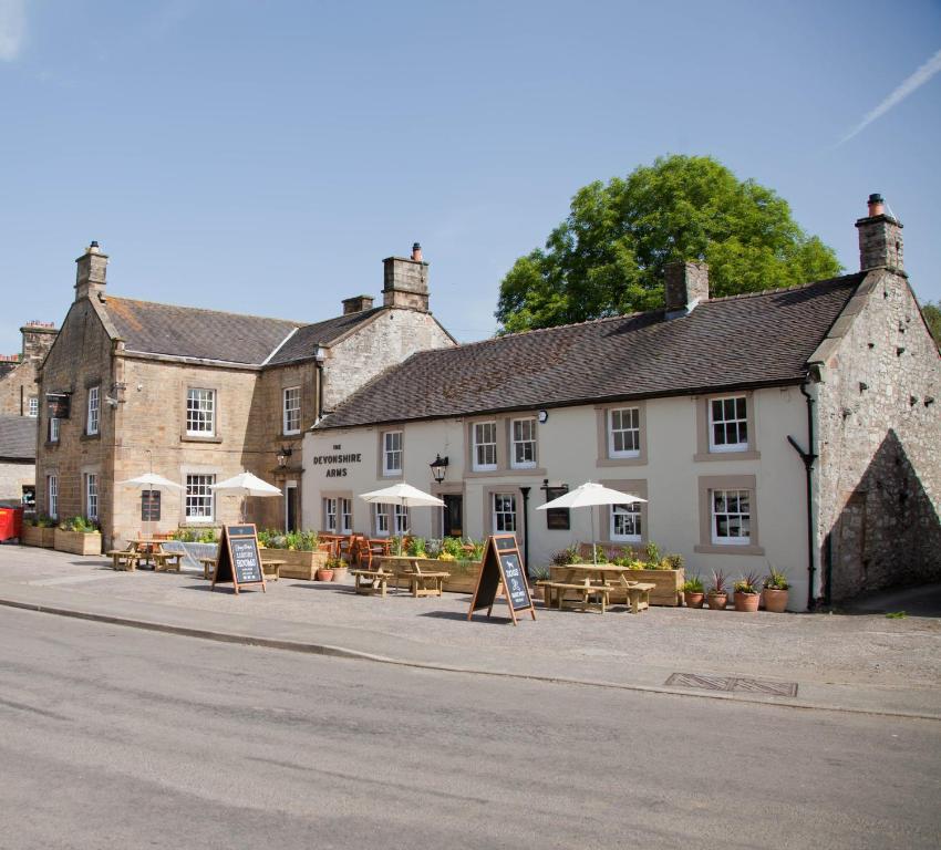 un bâtiment avec des tables et des parasols devant lui dans l'établissement Devonshire Arms, à Hartington