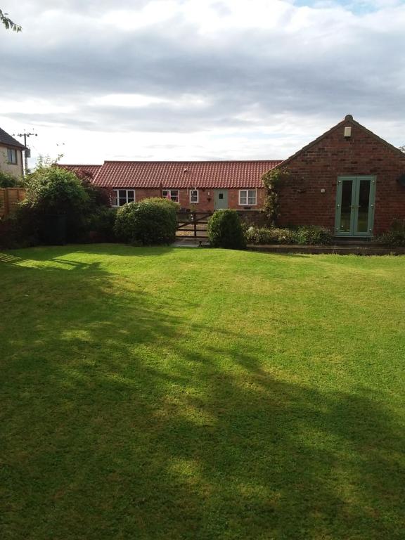 um grande quintal com um edifício de tijolos e um campo de relva em Wren Cottage em Louth