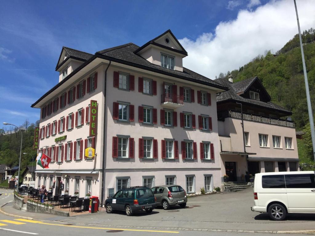 um grande edifício branco com carros estacionados em frente em Hotel Alpina em Unterschächen