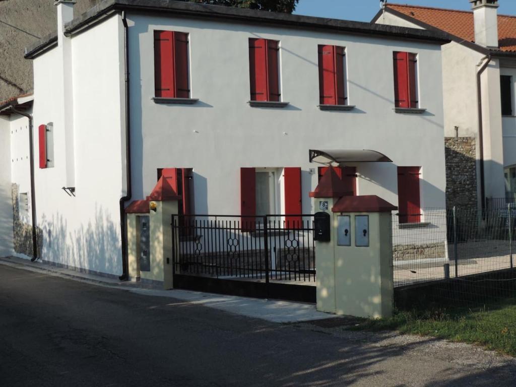 a white house with red windows and a fence at Casa Rossa in Pianzano