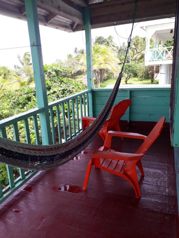 dwa czerwone krzesła i hamak na ganku w obiekcie Corn Island Hostal ALAL SUITE w mieście Corn Islands