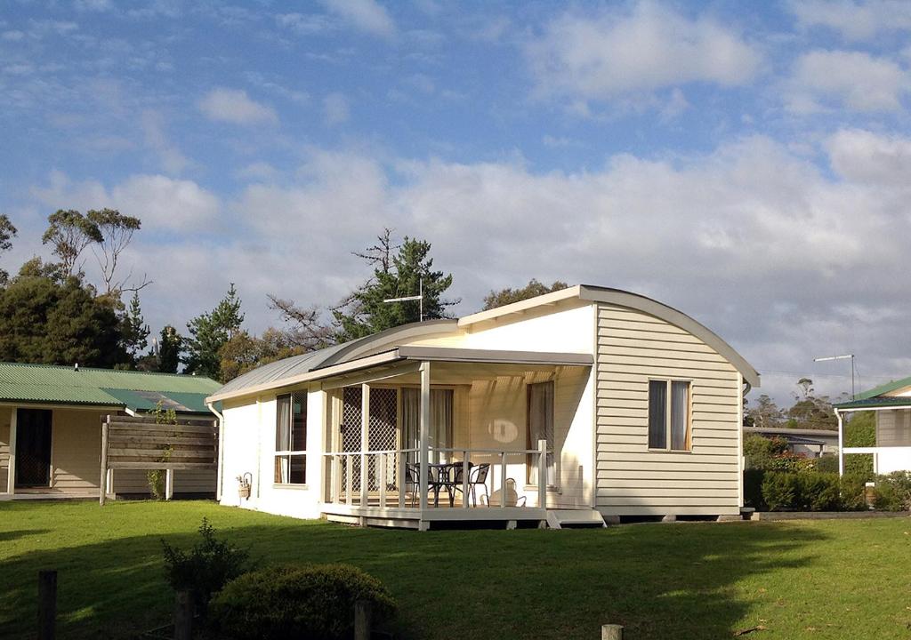 a small white house with a porch on a lawn at Beauty Point Tourist Park in Beauty Point