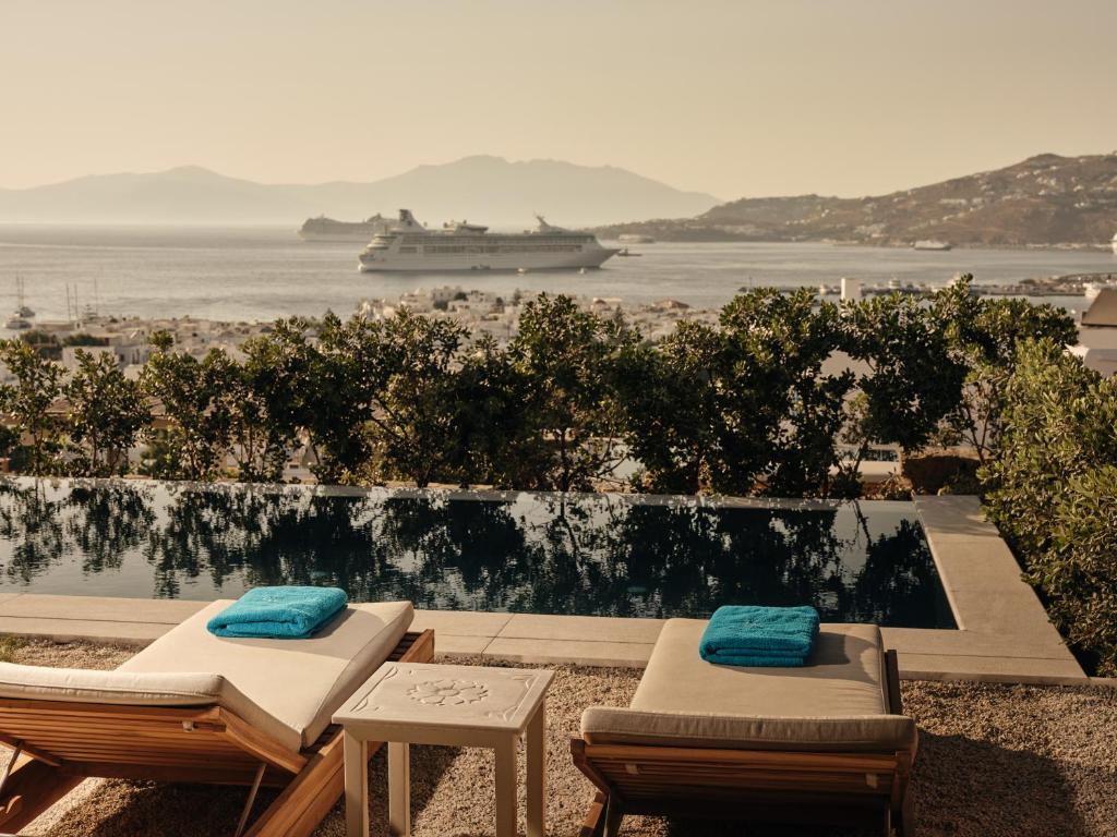 two lounge chairs and a cruise ship in the water at Belvedere Mykonos - Hilltop Rooms & Suites - The Leading Hotels of the World in Mikonos