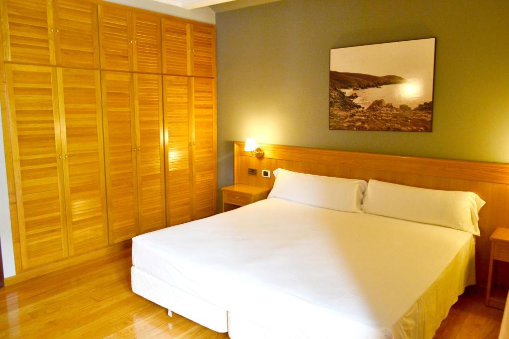 um quarto com uma cama branca e armários de madeira em Hotel Alda El Suizo em Ferrol