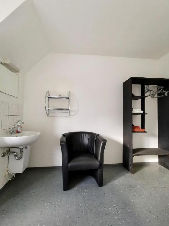ein Badezimmer mit einem schwarzen Stuhl und einem Waschbecken in der Unterkunft Pension Akropolis in Rellingen
