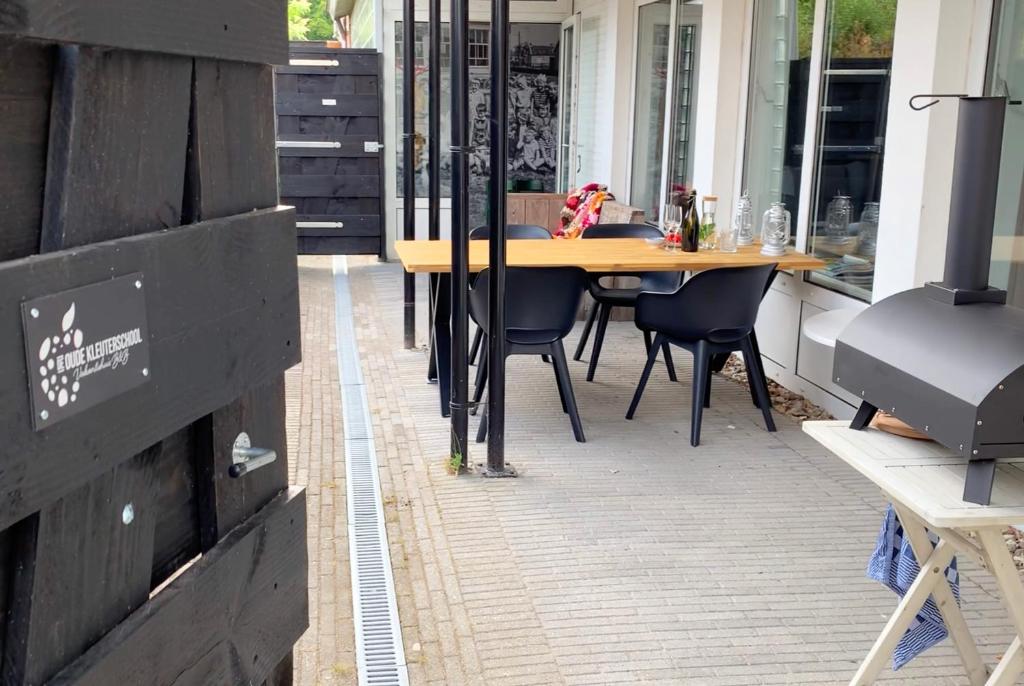 un patio con una mesa de madera y sillas. en De Oude Kleuterschool en Zoelen