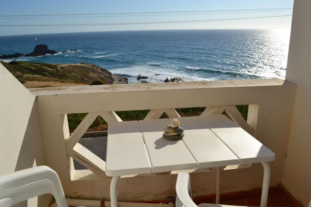 un tavolo bianco e sedie su un balcone con vista sull'oceano di Our Sunset Spot a Zambujeira do Mar