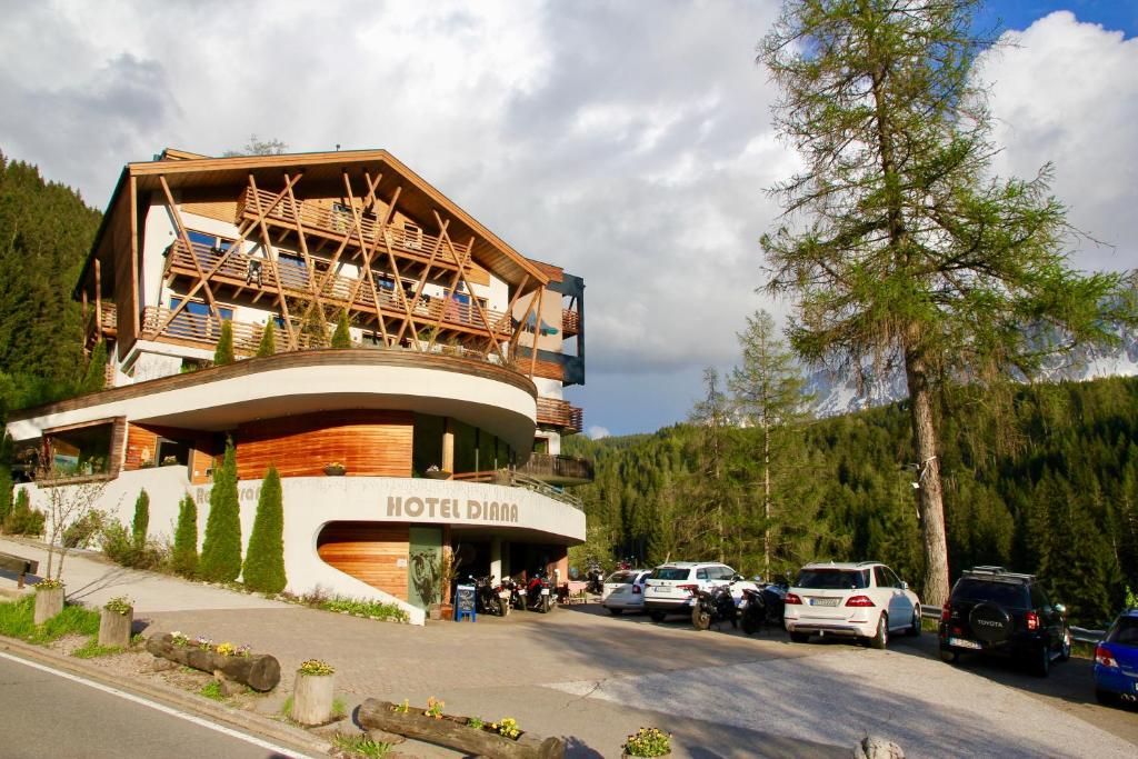 a hotel building with cars parked in a parking lot at Bike & Ski Hotel Diana in Nova Levante