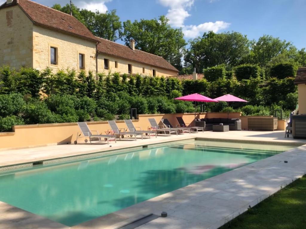 a swimming pool with chairs and umbrellas next to a building at Les Maisons du Cheylard-Lascaux in Les Farges