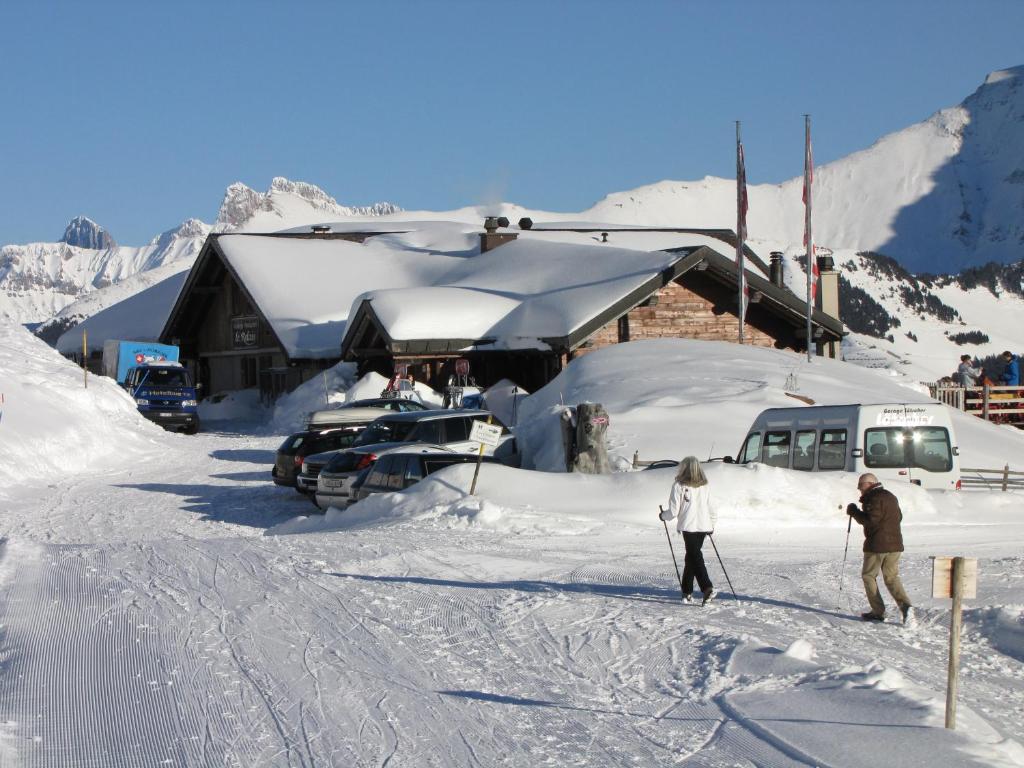 twee mensen op ski's in de sneeuw voor een lodge bij Hotel-Restaurant le Relais Panoramique in Les Crosets