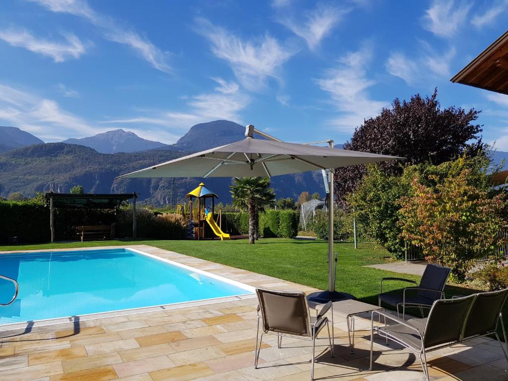 una piscina con sillas, una sombrilla y un parque infantil en Haus Winkler, en Vilpiano