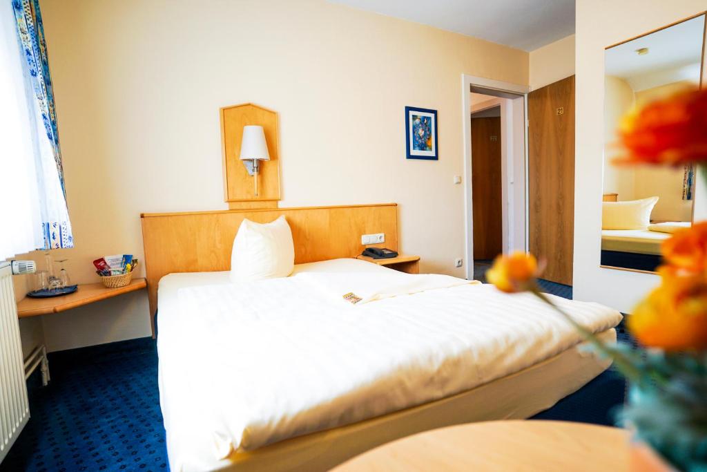 a hotel room with a white bed and a mirror at Hotel Sauer Garni in Neu Isenburg