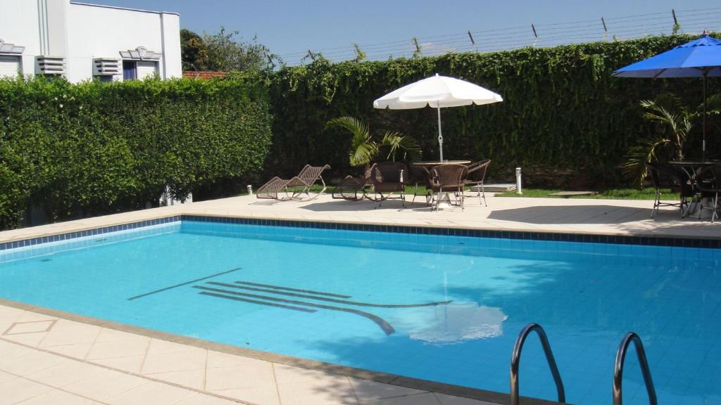 uma piscina azul com guarda-sol e cadeiras em Hotel Aero Park e Estacionamento em Londrina