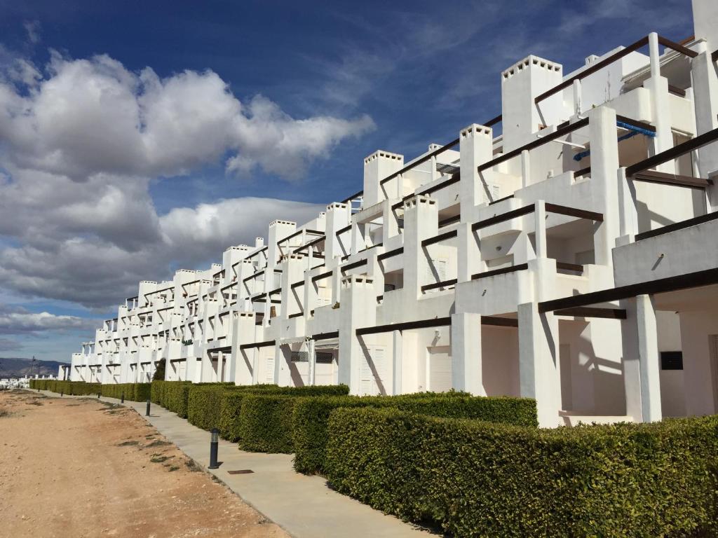 a white building with green bushes next to a road at Fairway View Penthouse in Murcia