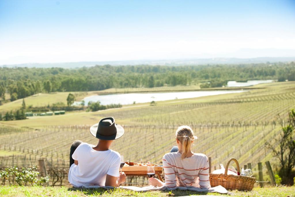 un hombre y una mujer sentados en la hierba mirando un viñedo en Audrey Wilkinson Vineyard en Pokolbin