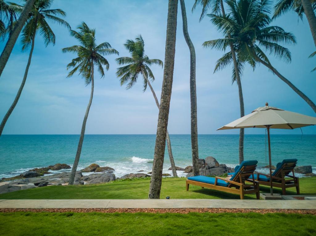 una playa con 2 sillas y una sombrilla y el océano en Bay Villas Balapitiya en Balapitiya