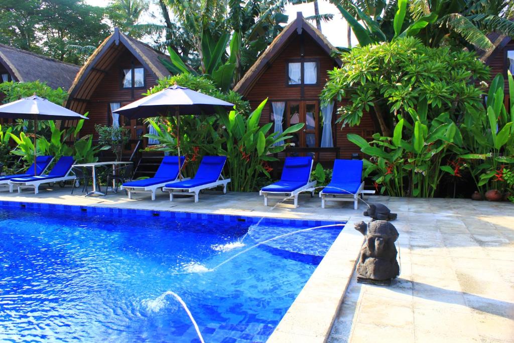 a pool with chairs and umbrellas next to a house at Turtle Beach Hotel in Gili Air