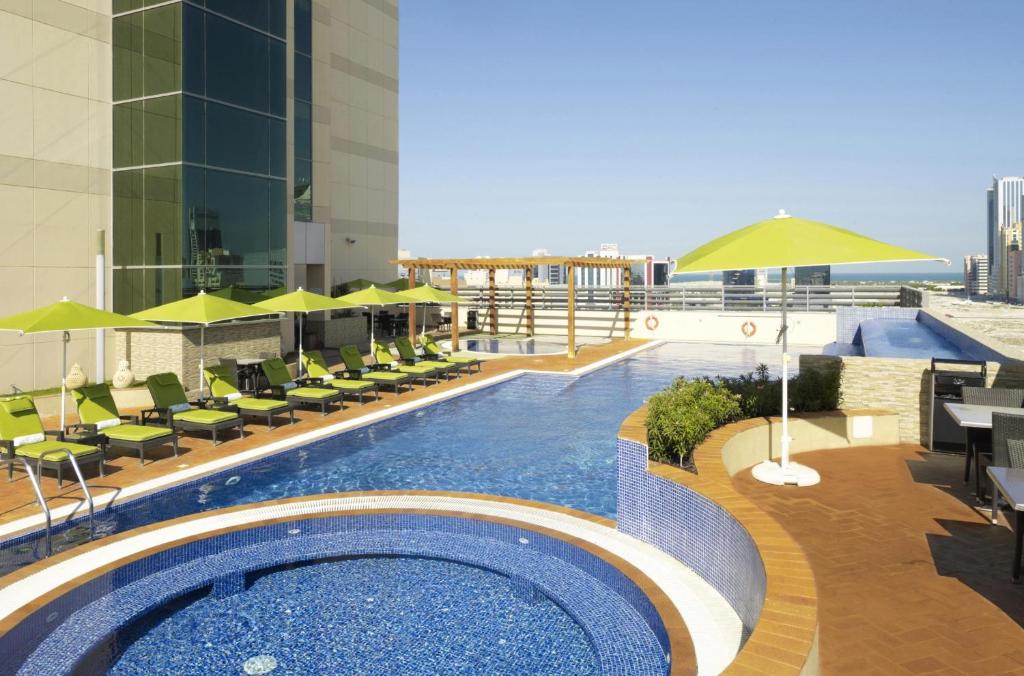 a swimming pool with chairs and umbrellas on a building at Fraser Suites Seef Bahrain in Manama