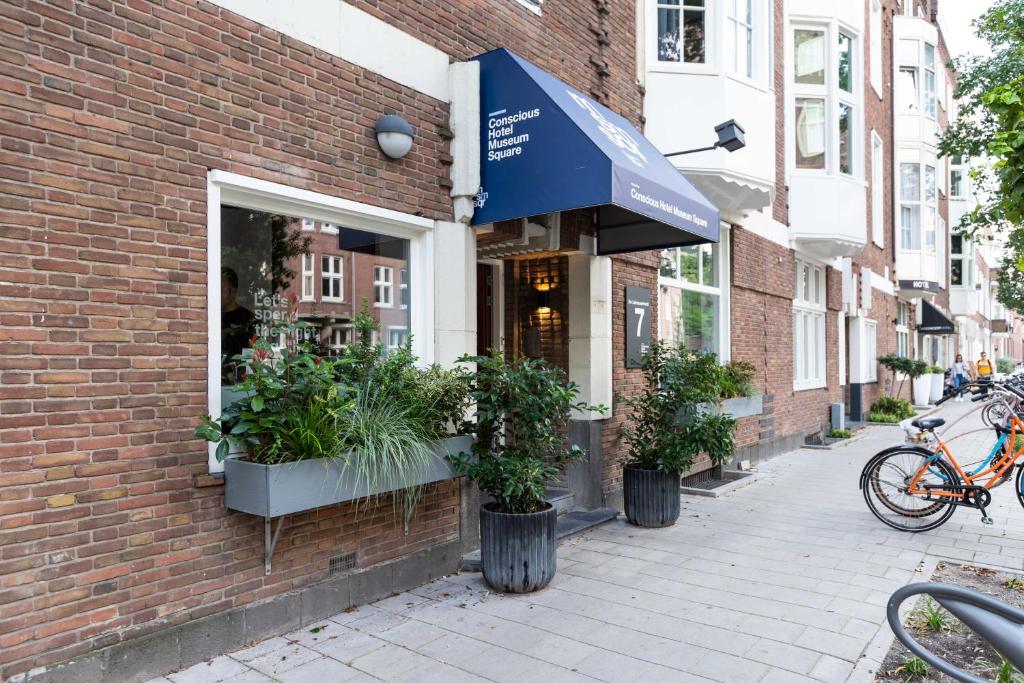 a brick building with plants in pots on a sidewalk at Conscious Hotel Museum Square in Amsterdam