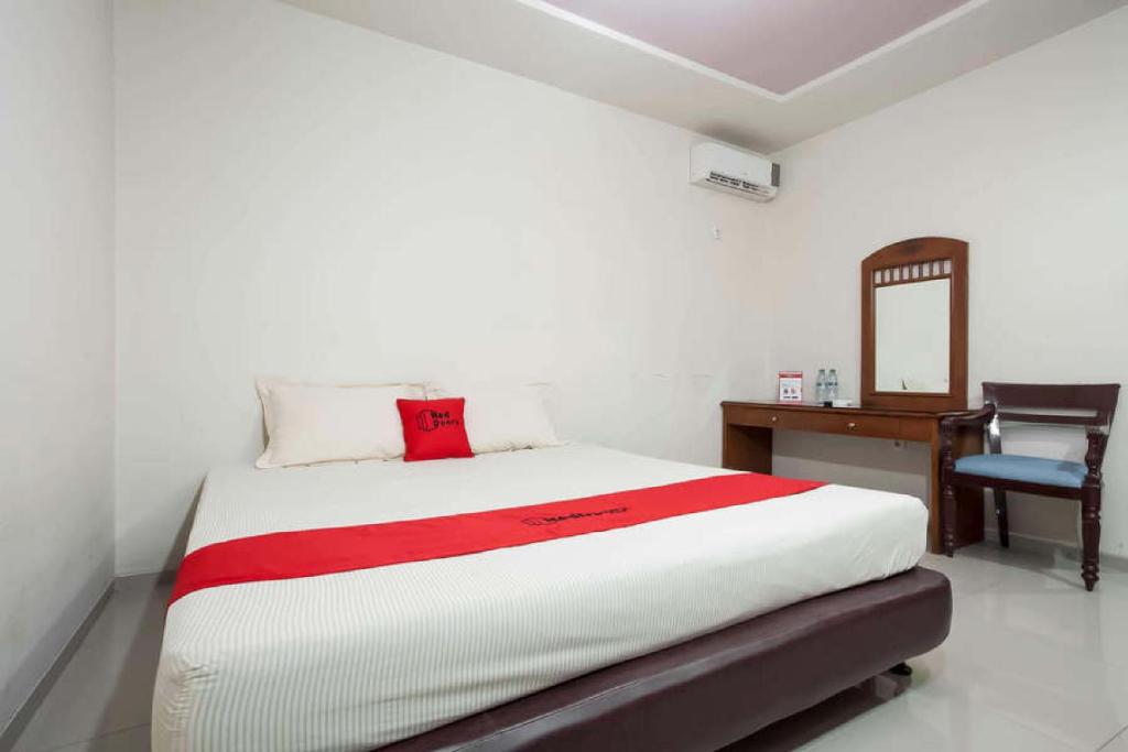 1 dormitorio con cama, escritorio y espejo en RedDoorz @ Panglima Sudirman, en Surabaya