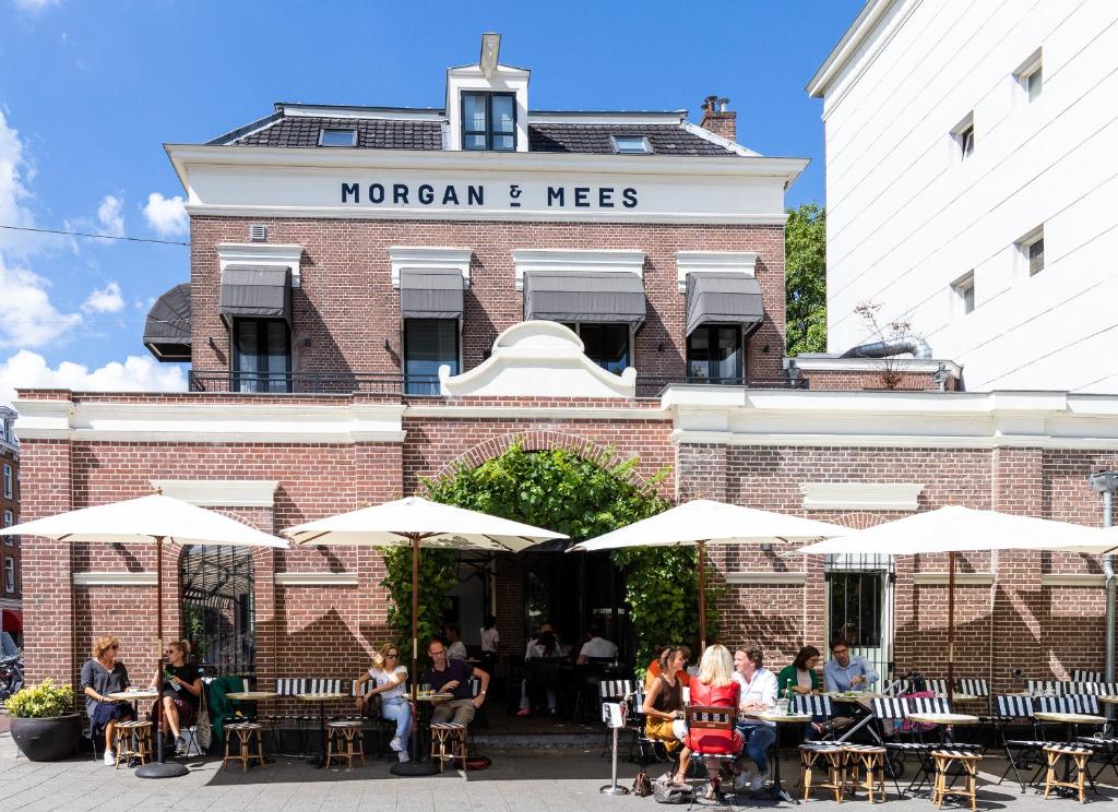 een groep mensen die aan tafels voor een gebouw zitten bij Morgan & Mees Amsterdam in Amsterdam