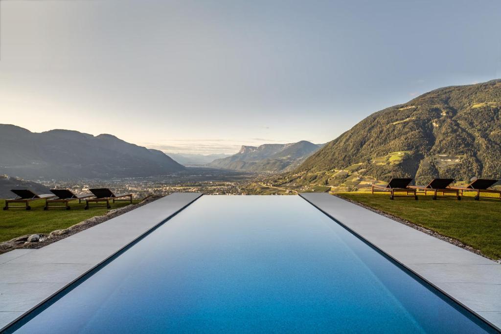 uma piscina de beiral infinito com cadeiras e montanhas ao fundo em Arua Private Spa Villas em Merano