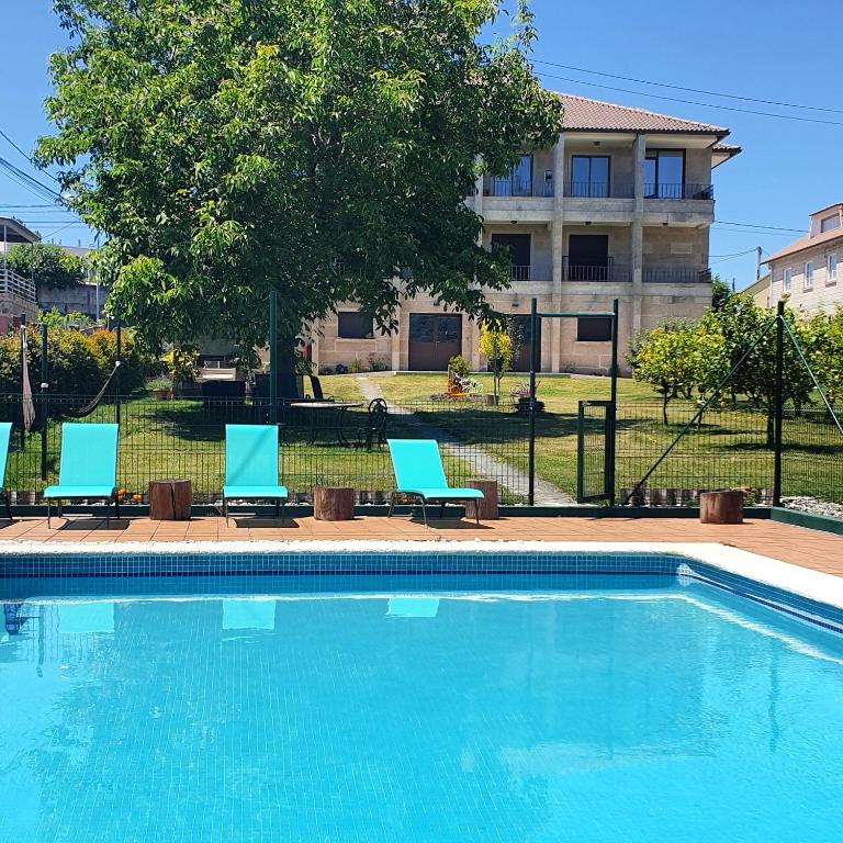 a swimming pool with three chairs and a building at Apartamentos Ria de Aldan in Aldán