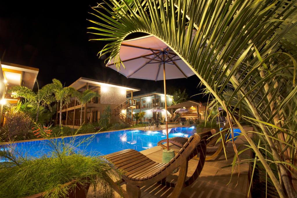 a bench with an umbrella next to a swimming pool at night at Pousada Canto do Sol in Barra Grande