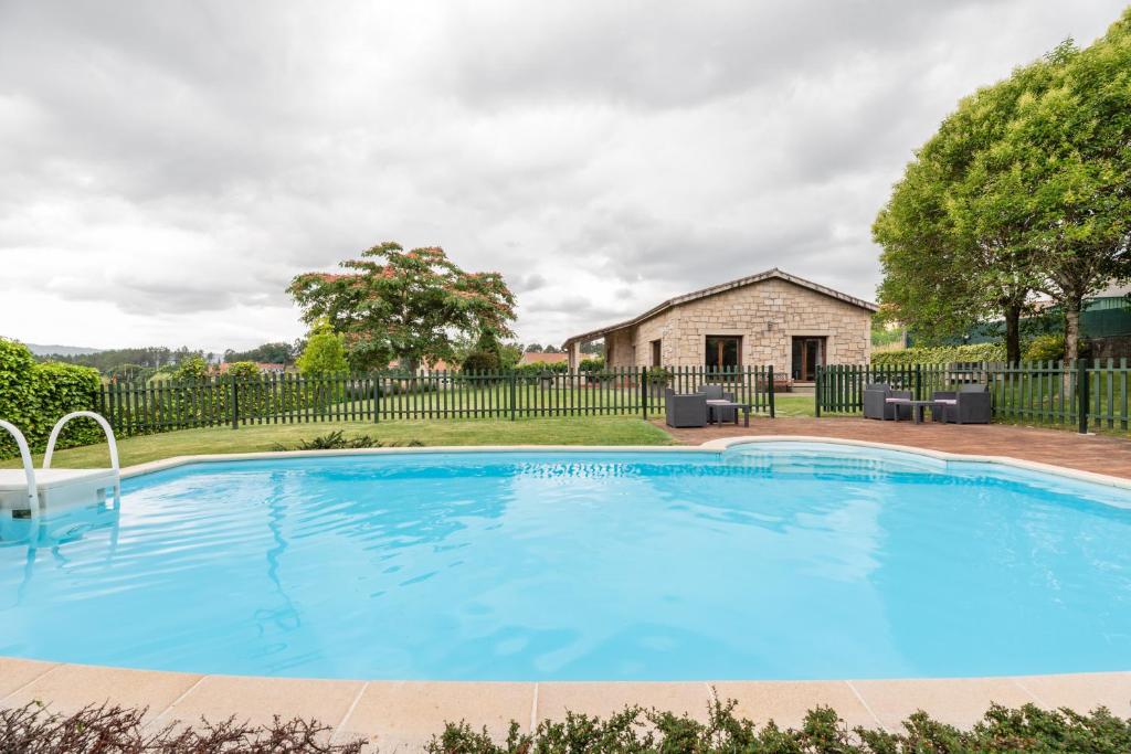 uma grande piscina azul em frente a uma cerca em Casa A Pedriña em Amés