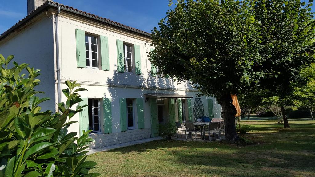 una casa blanca con persianas verdes y un árbol en Chez Alexandra, en Louchats