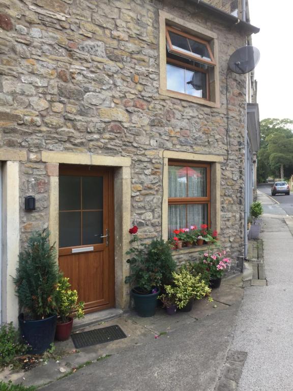 a stone house with a wooden door and some plants at Little Pinfold Cottage in Skipton