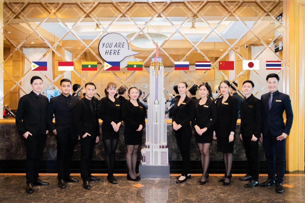 Hotel staff pose in a polished lobby beneath international flags and a central “You are here” sign.