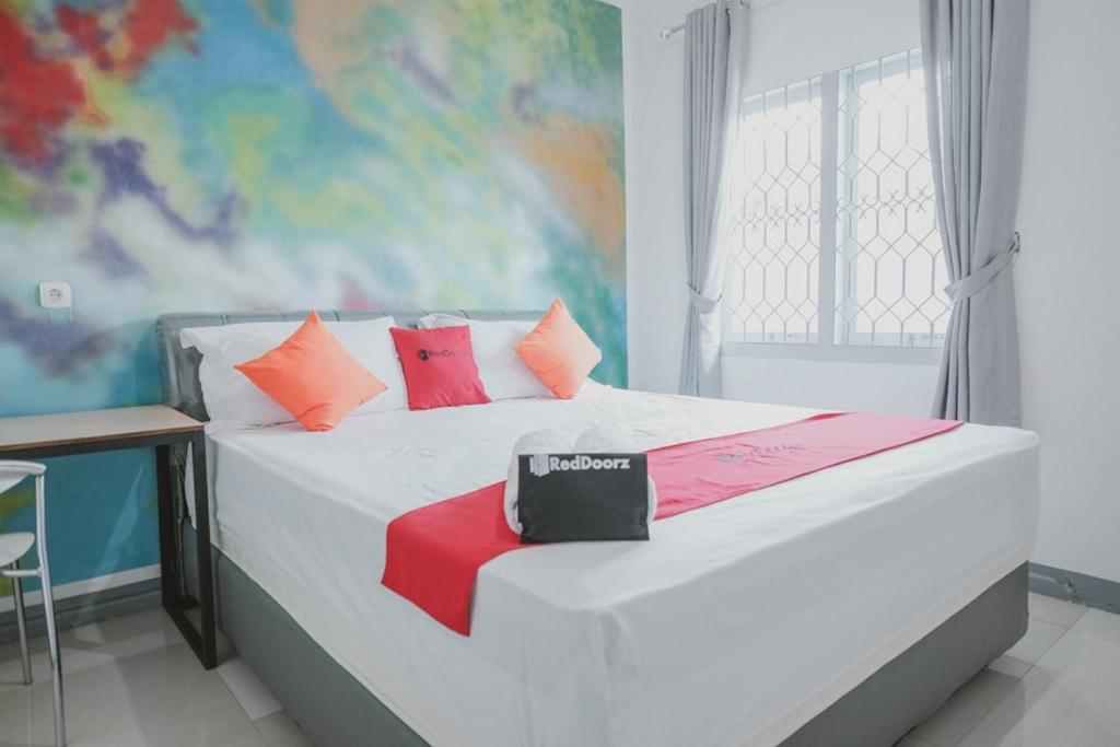 1 dormitorio con cama blanca y almohadas coloridas en RedDoorz @ Beringin Jambi, en Palmerah