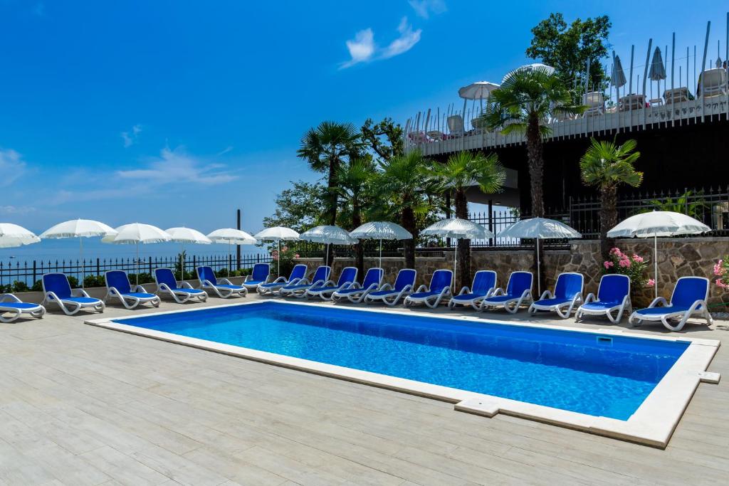 a pool with chairs and umbrellas next to the ocean at Hotel Domino in Opatija