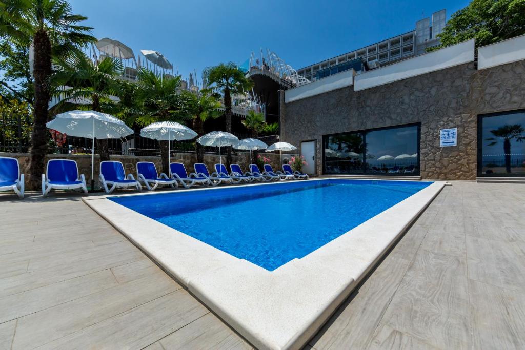 a swimming pool with blue chairs and umbrellas at Hotel Domino in Opatija