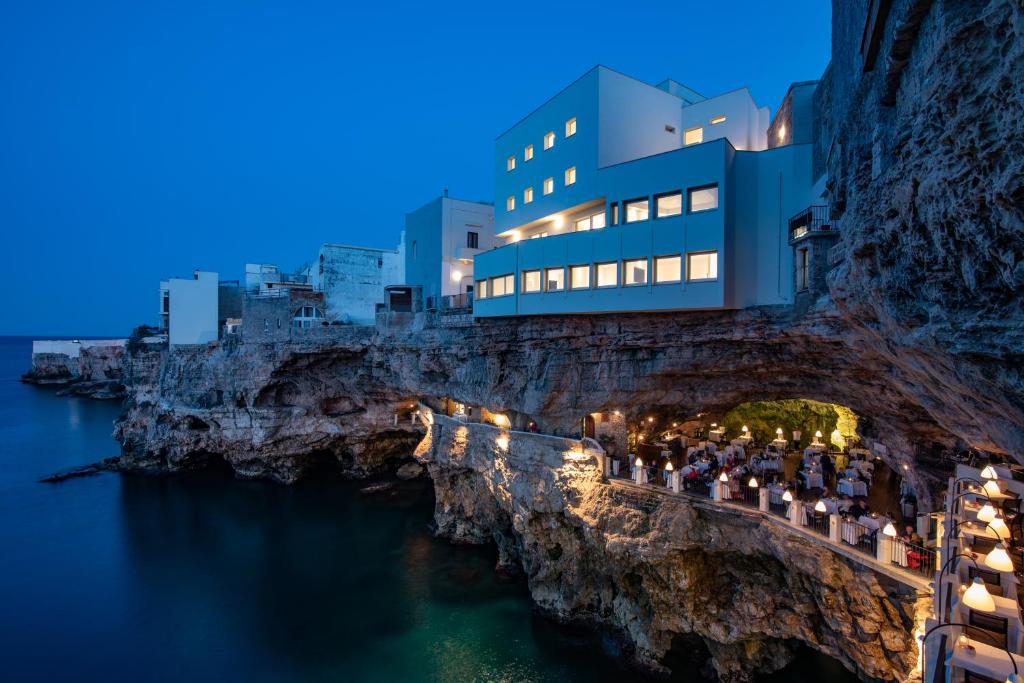 Hotel Grotta Palazzese في بولينيانو آ ماري: مبنى على منحدر بجوار الماء ليلا