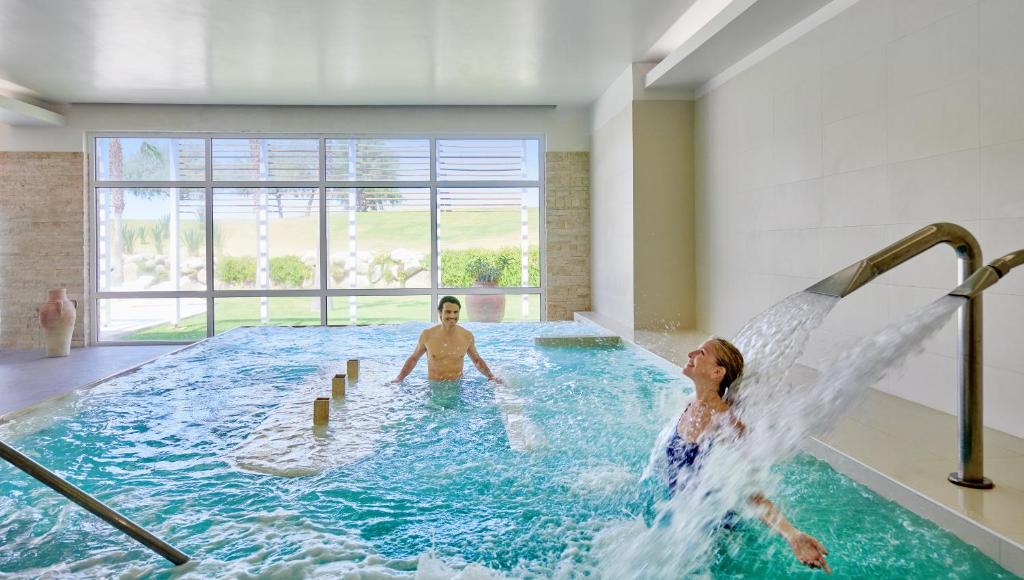 a man and a woman in a swimming pool at Capovaticano Resort Thalasso Spa in Capo Vaticano