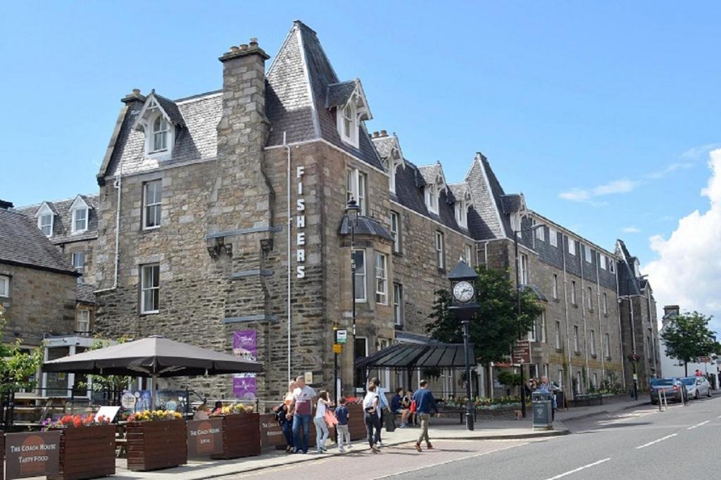 um grande edifício de pedra com um relógio ao lado de uma rua em Fisher's Hotel em Pitlochry