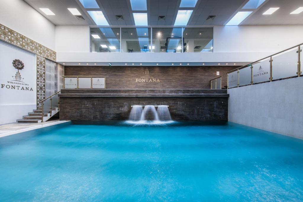 a pool of blue water in a building with a waterfall at Hotel Fontana Vrnjačka Banja in Vrnjačka Banja