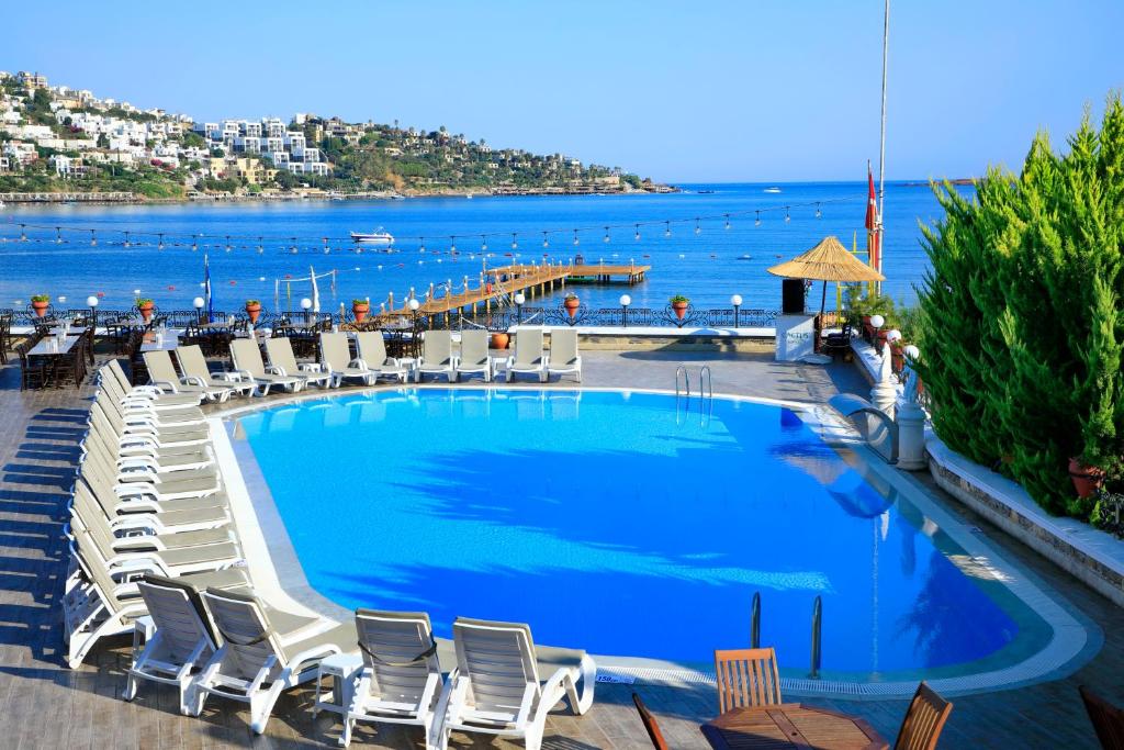 a swimming pool with chairs and the ocean in the background at Cactus Fleur Beach in Yalıkavak