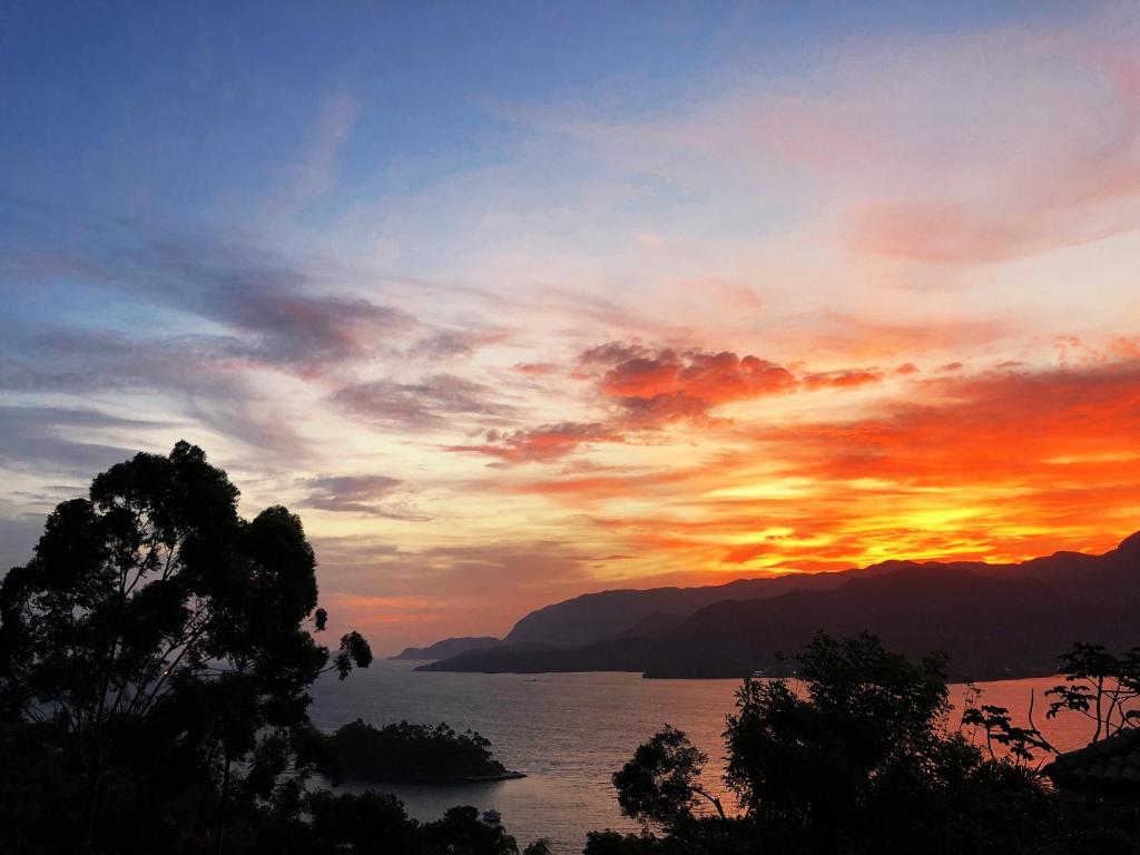 um pôr-do-sol sobre um corpo de água com montanhas em CASA PIÚVA em Ilhabela