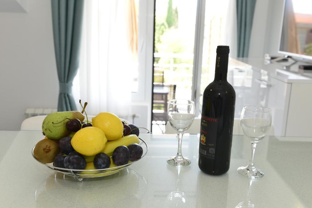 a bottle of wine and a bowl of fruit on a table at Apartmani Stefanija in Tivat