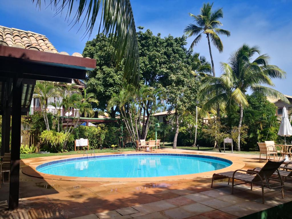 a pool at a resort with chairs and palm trees at Apartamento Solar do Forte - Praia do Forte in Praia do Forte