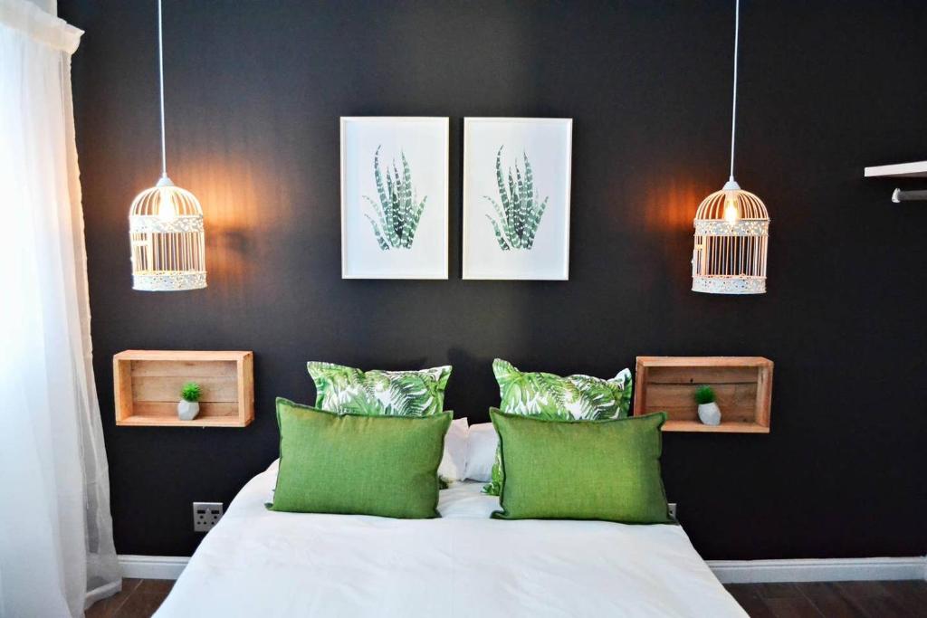 Un dormitorio con una cama con almohadas verdes y pinturas en Aintree Farm Cottage, en Langebaan