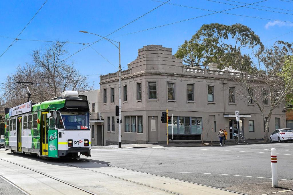 a bus driving down a street in front of a building at Plum Serviced Apartments North Melbourne in Melbourne