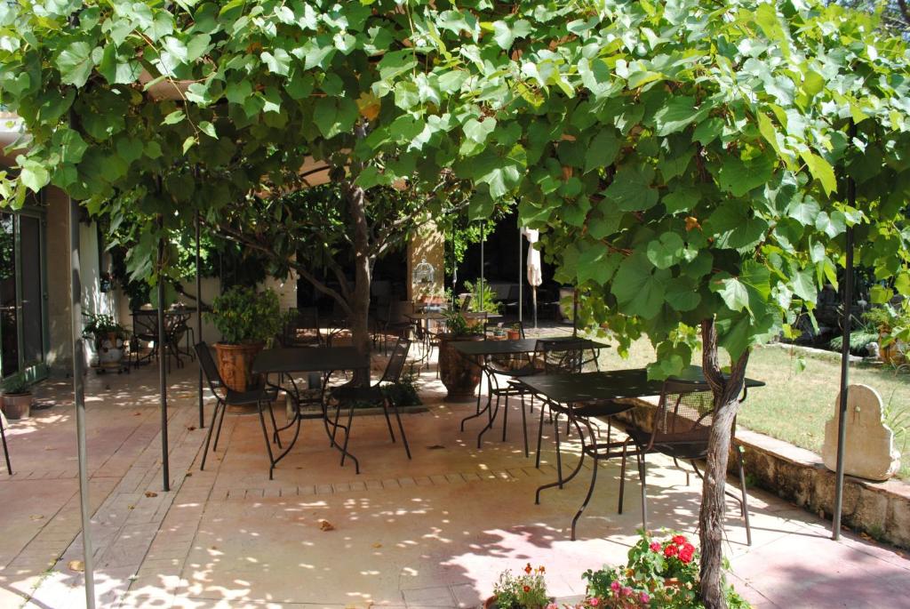 a patio with tables and chairs under a tree at Mas de Bouvau in Violès
