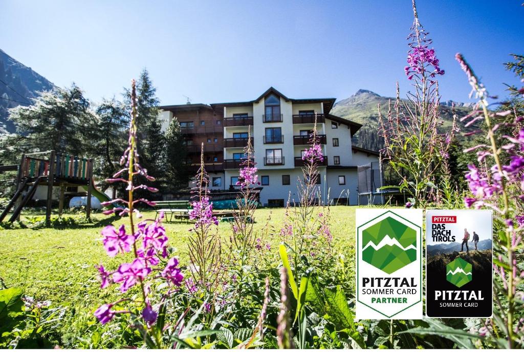 un cartel en un campo con flores delante de un edificio en Hotel Gletscherblick en Sankt Leonhard im Pitztal