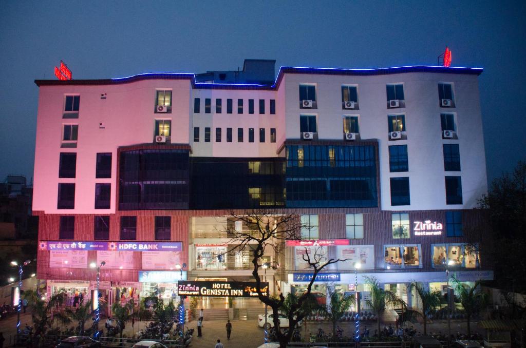 Un grand bâtiment blanc avec des lumières allumées la nuit dans l'établissement Hotel Genista Inn, à Rānchī