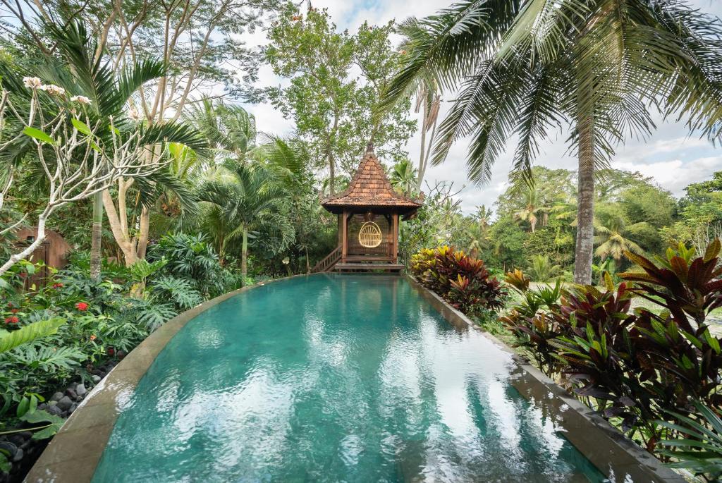 a swimming pool in a garden with a clock in it at Villa Uma Anyar- Joglo Uma in Ubud